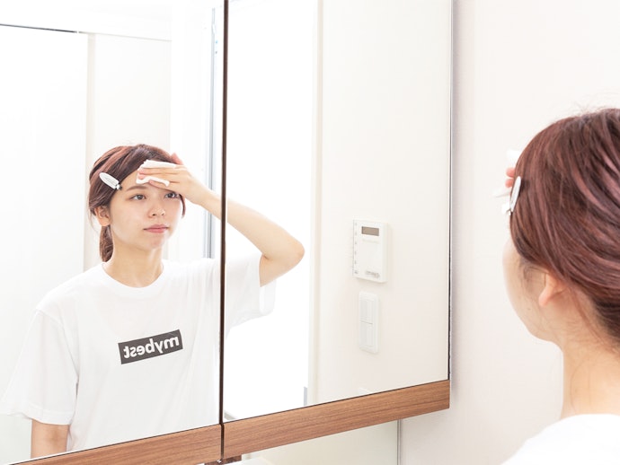 女性が鏡の前で化粧水をおでこに塗っている