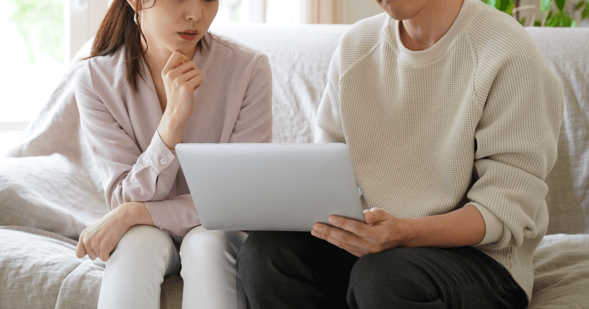 男女がソファに座ってノートパソコンを見て話しをしている