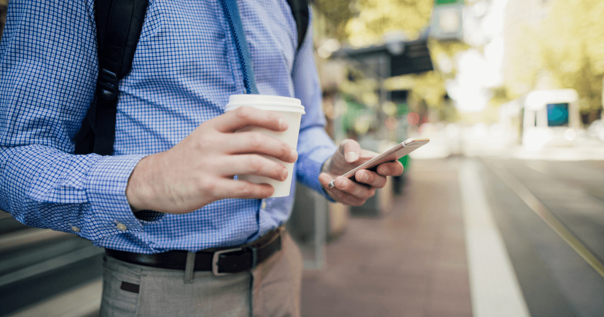 片手にコーヒーを持ちながらスマホを操作している